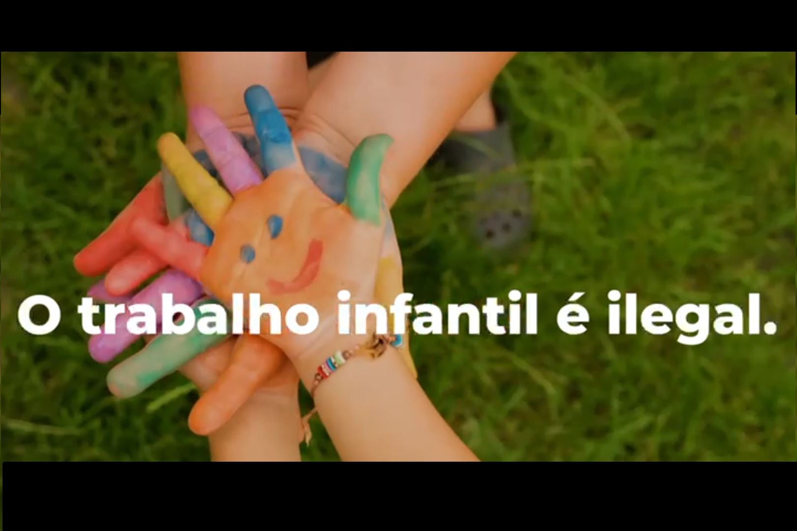Foto de um frame do vídeo com a imagem de mãos de crianças pintadas com tinta e a frase "o trabalho infantil é ilegal"