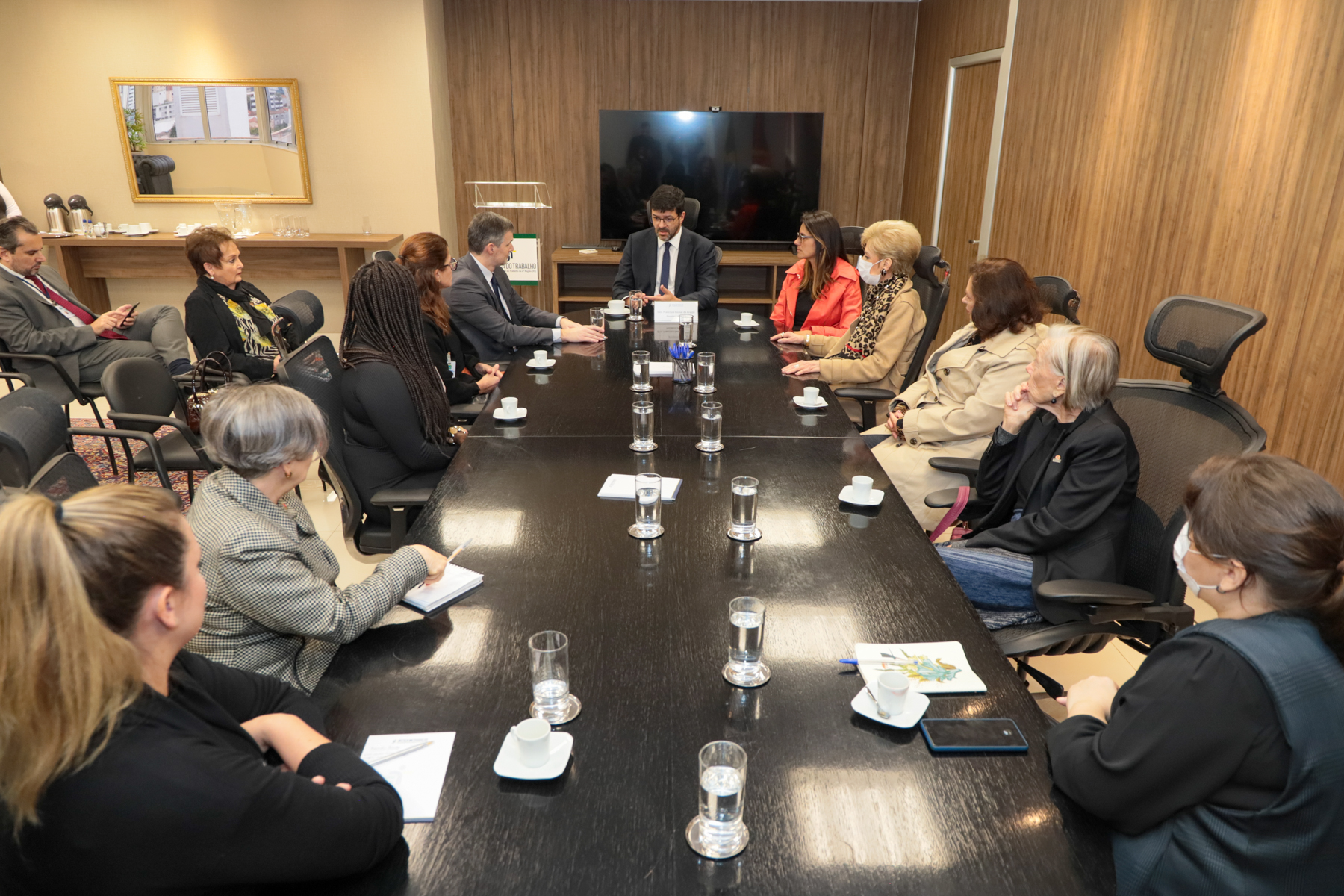 Foto da reunião, mostrando os participantes conversando, sentados à mesa do Salão Nobre