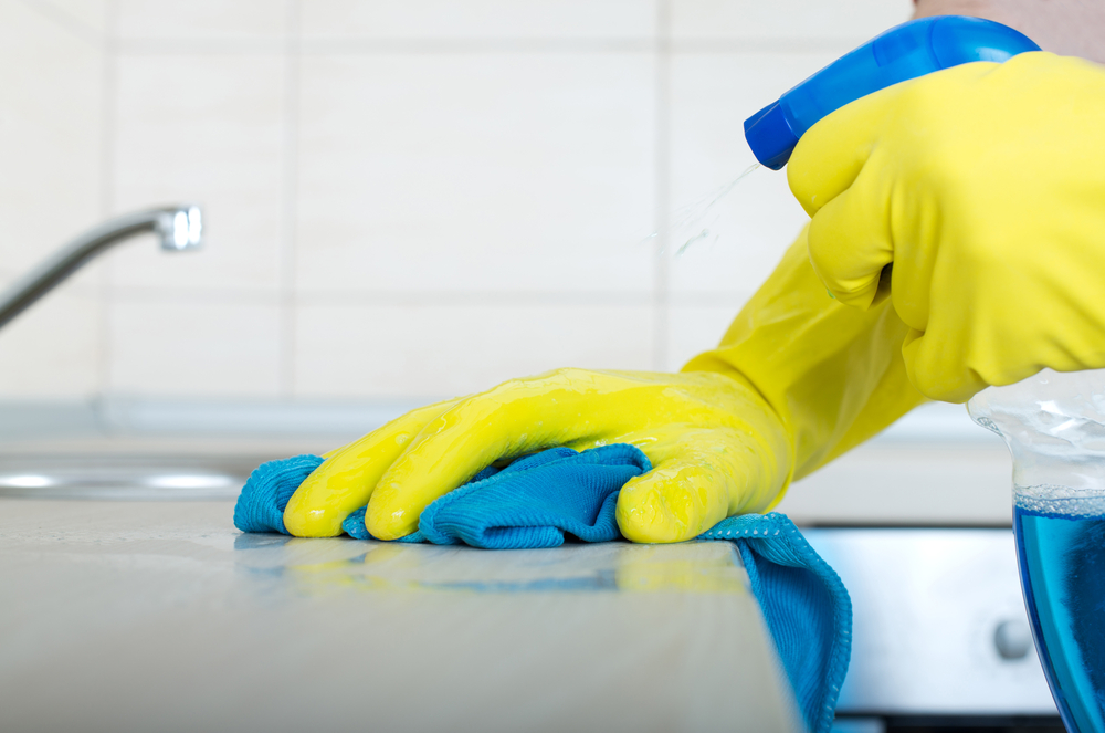 Foto, em ângulo fechado, de uma pessoa, com luvas, limpando um balcão de pia de cozinha.
