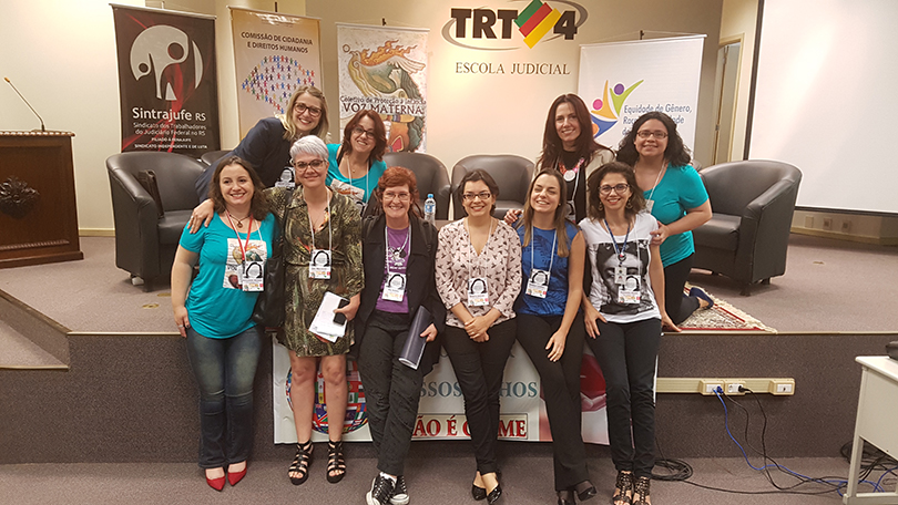 Fotografia mostra grupo de mulheres posando em frente ao palco do Auditório Ruy Cirne Lima da Escola Judicial do TRT-RS