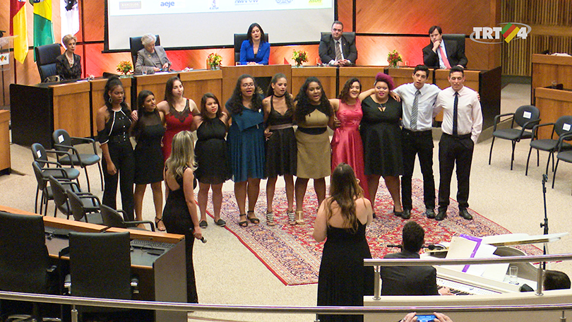 Fotografia mostra alunos abraçados, um ao lado do outro, ao centro do Plenário Milton Dutra, no TRT-RS