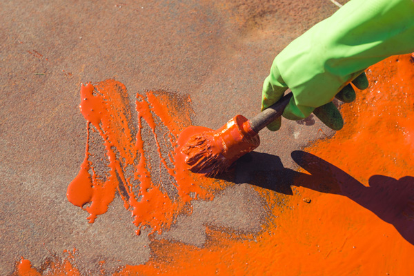 Foto de uma mão com luva pintando de tinta amarela fundo com textura de metal áspero (desgastado).