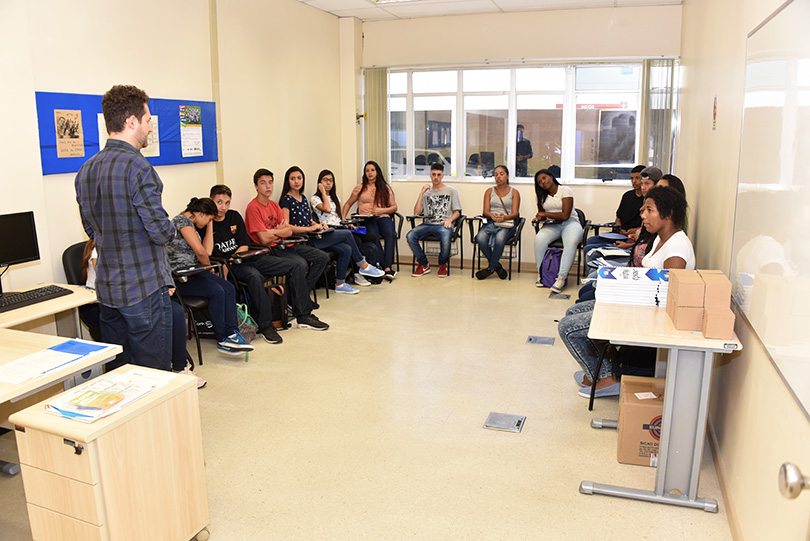 Fotografia de jovens em sala de aula com um instrutor falando a sua frente