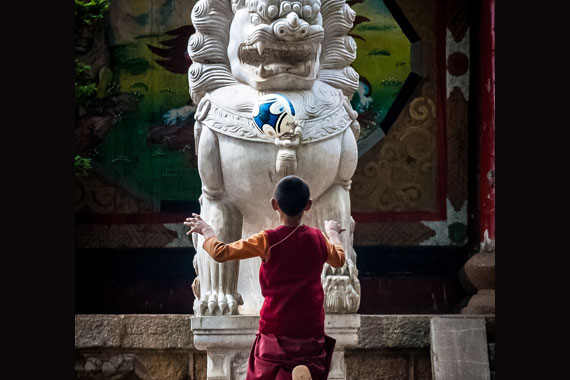 Imagem vencedora a categoria Sintrajufe/RS. Mostra uma criança budista de costas, brincando com uma bola de futebol (no ar, sobre a cabeça da criança), em frente a uma estátua.