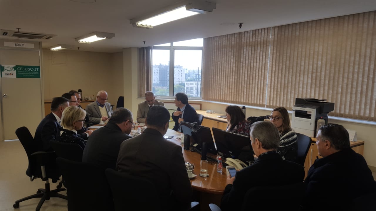 Sala de reuniões com a mesa em primeiro plano com representantes dos sindicatos e a Federação dos Metalúrgicos