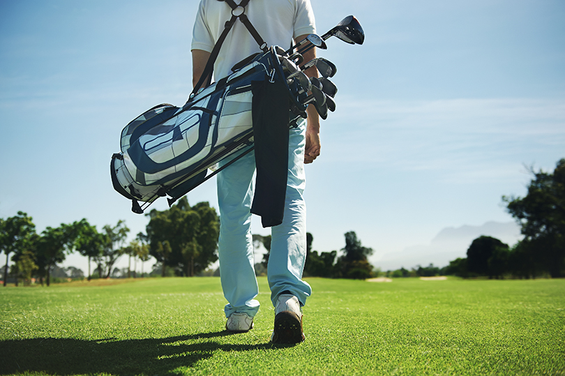 Foto de homem de costas carregando tacos de golfe em uma bolsa