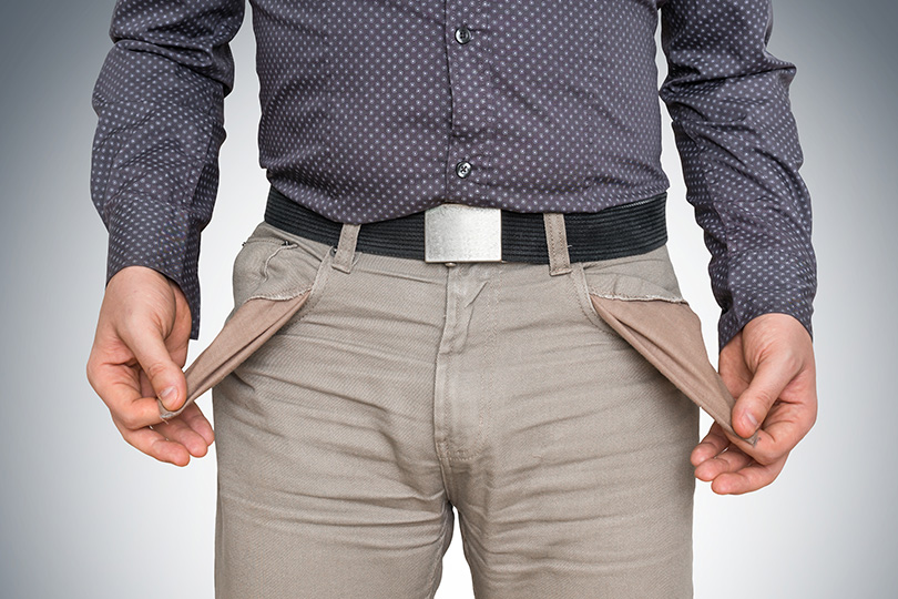 Fotografia de homem puxando os bolsos vazios da calça para fora, imagem típica de falta de dinheiro.