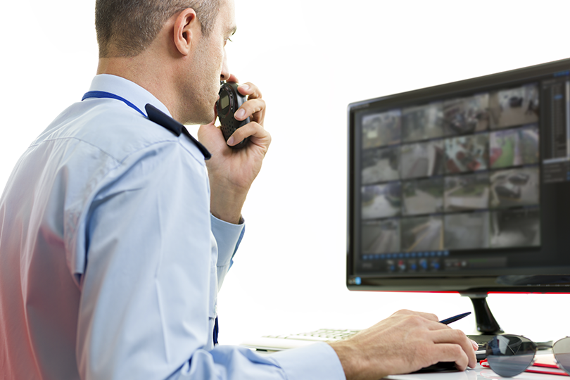 Imagem de um guarda de segurança controlando uma central de monitoramento