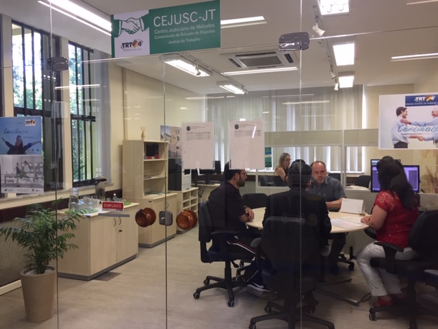 Imagem da entrada do Cejusc, mostrando audiências sendo realizadas nas duas mesas