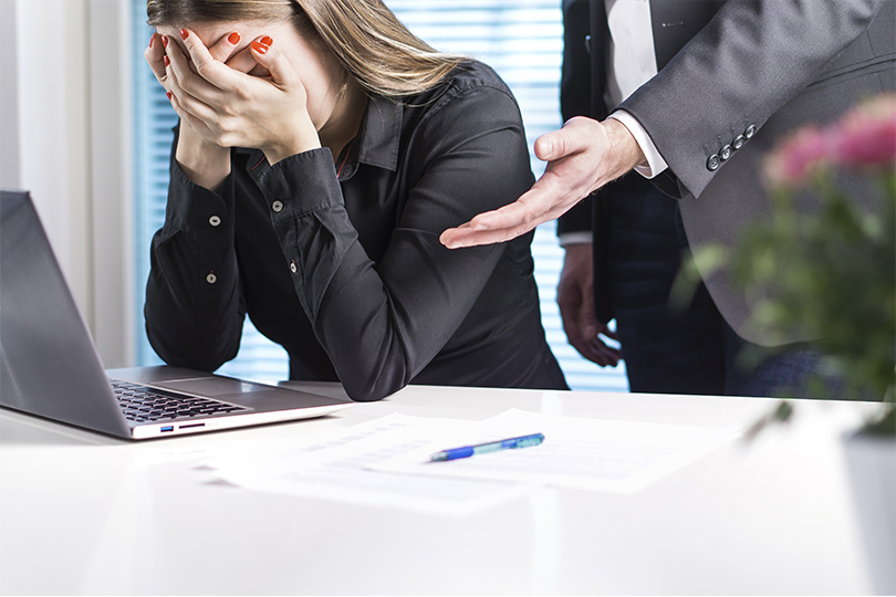 Mulher está sentada à mesa chorando enquanto seu chefe a repreende.