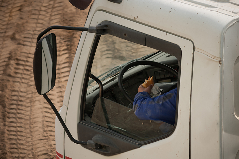Fotografia de um trabalhador comendo um sanduiche dentro de um caminhão