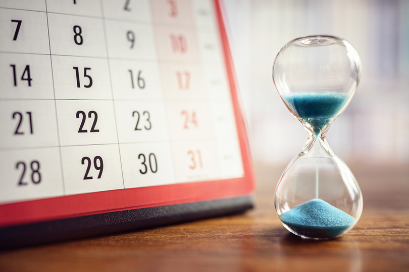 Fotografia de uma ampulheta em frente a um calendário