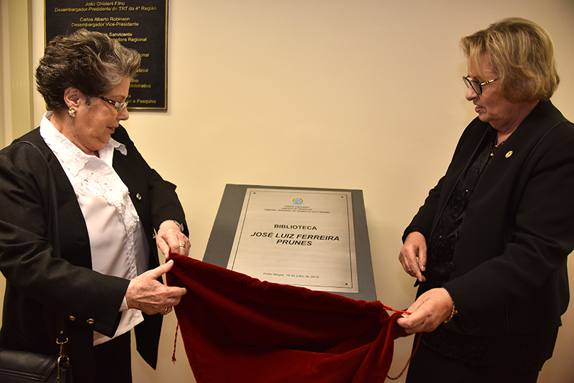 Foto de Lúcia Mendes Prunes e da presidente Vania Mattos descerrando a placa em homenagem ao desembargador José Luiz Ferreira Prunes.