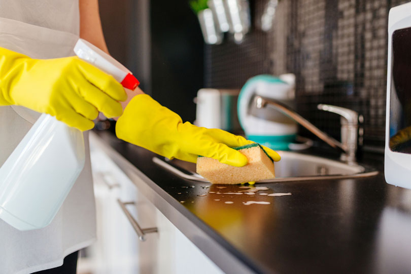 Foto de uma empregada doméstica limpando a pia de uma cozinha.