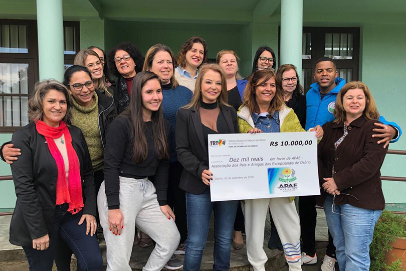 Foto posada da juíza Silvana Martinez de Medeiros com representantes da Apae de Osório. Ela segura um papel com o valor de R$ 10 mil e o logo do TRT-RS, simbolizando um cheque.