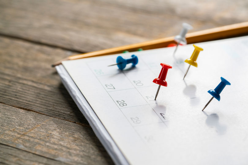 Imagem de um calendário sobre uma mesa, com tachinhas coloridas marcando alguns dias.
