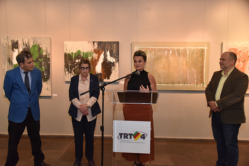Foto da cerimônia de inauguração, com o vice-presidente Ricardo Fraga, a presidente Vania Mattos, a pintora Raquel Boufleur, o desembargador João Paulo Lucena e os quadros ao fundo.