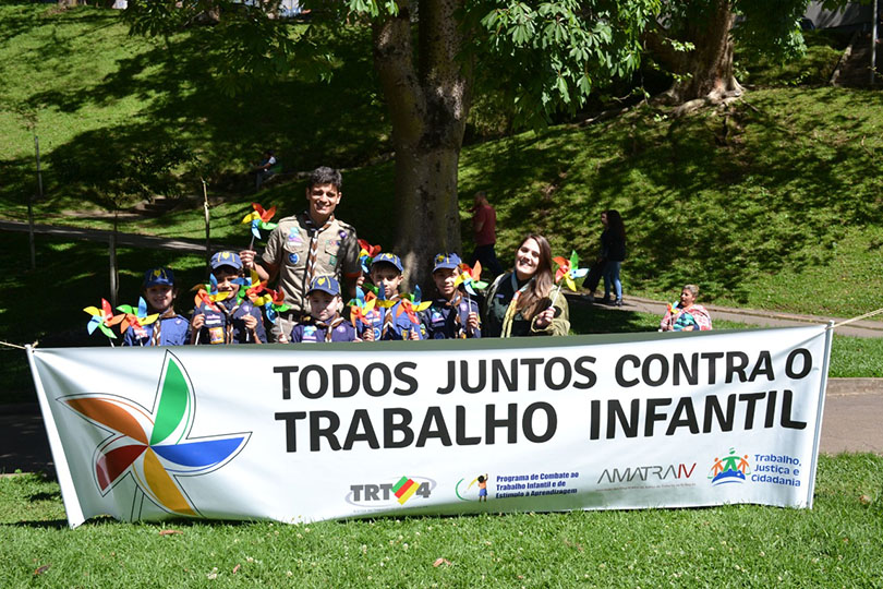 Fotografia de escoteiros junto de algumas crianças com um banner da campanha contra o trabalho infantil