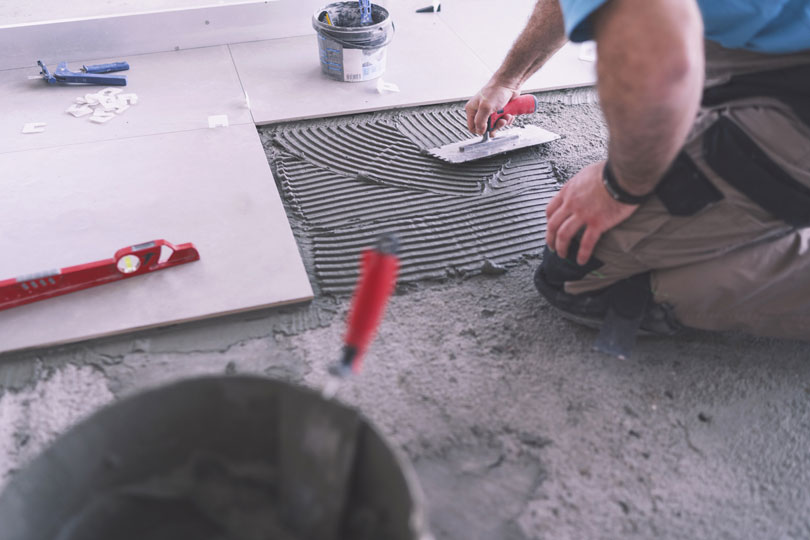 Foto de um trabalhador assentando um piso em uma obra.