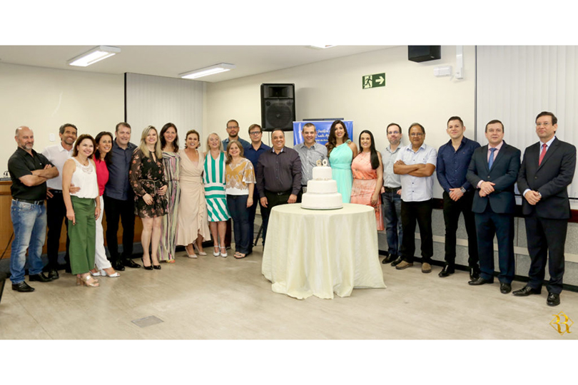 Foto posada de juízes, desembargadores, servidores e convidados durante celebração no Foro Trabalhista de Santa Maria. Há, em primeiro plano, um bolo em camadas em cima de uma mesa. Ele tem o número 60 no topo.