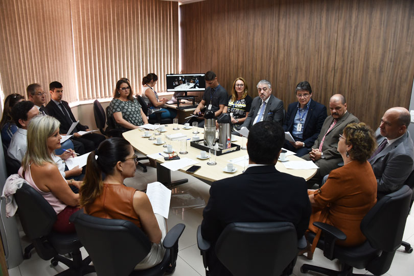 Foto em ângulo aberto, mostrando todos os participantes da reunião à mesa.