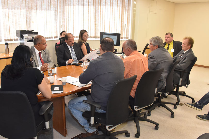 Juiz e representantes dos sindicatos de trabalhadores e de empresas reunidos em volta da mesa, na sala de audiências.