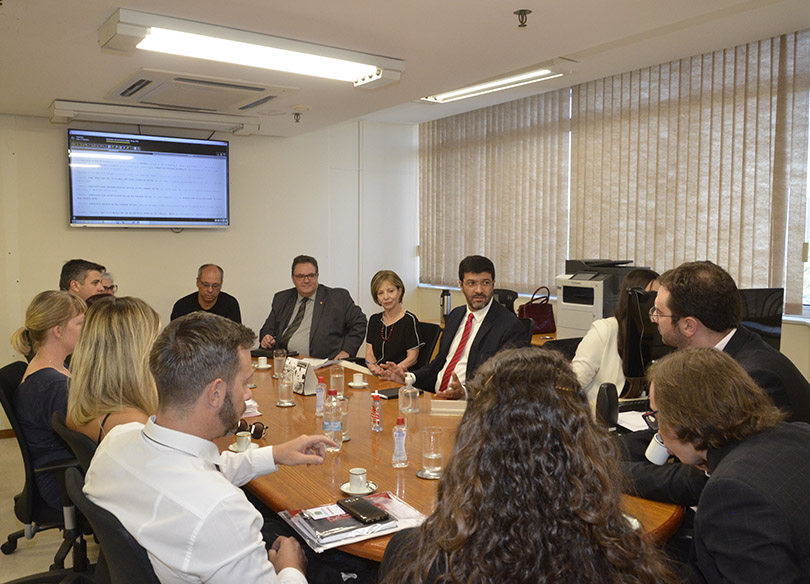 Advogados e partes reunidos com o vice-presidente do TRT-RS, desembargador Francisco Rossal de Araújo, ao redor da mesa, na sala de audiências.