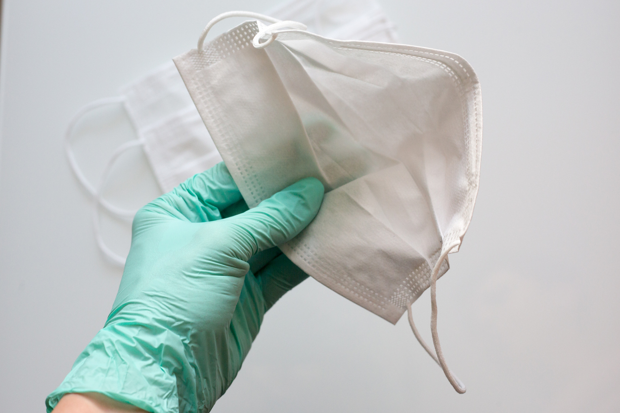 mão de profissional de saúde usando luva e segurando máscara
