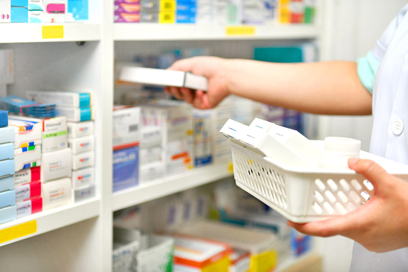 Foto de MJ_Prototype/IStock mostra um trabalhador repondo medicamentos em uma prateleira de farmácia.