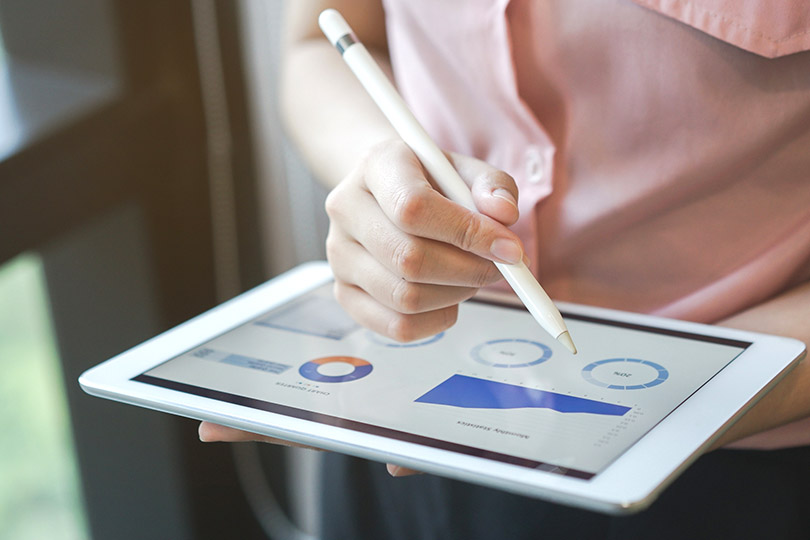 Pra Cego Ver: Foto de Chainarong Prasertthai,/Istock Banco de Imagens mostra uma mulher avaliando gráficos de resultados na tela de um tablet.