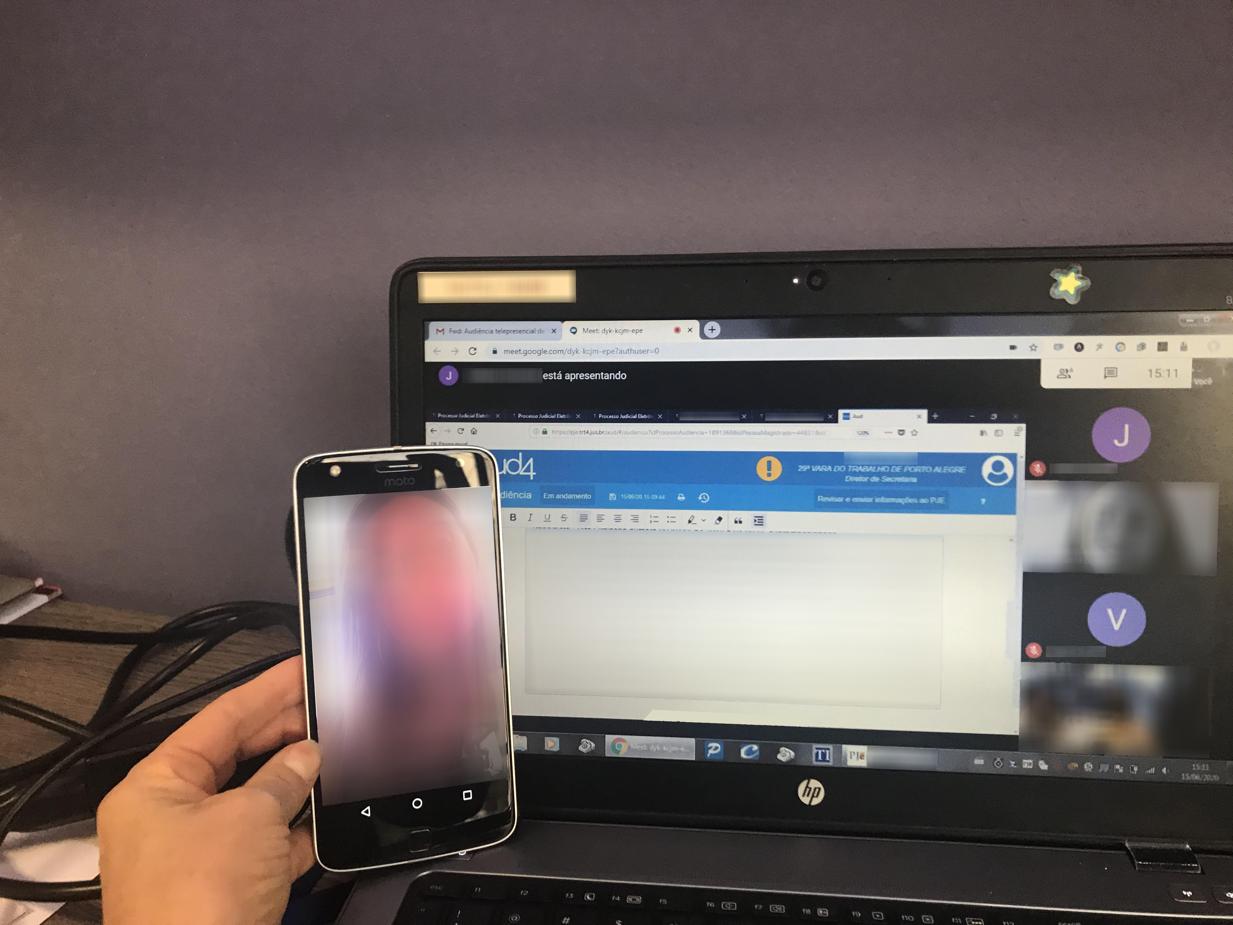 Em frente à tela do notebook onde aparecem os demais participantes da audiência, a juíza segura um celular que mostra a autora do processo