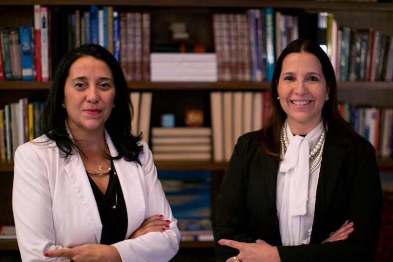 Juízas Maria Teresa e Maria Beatriz posam para a foto em frente a uma estante de livros