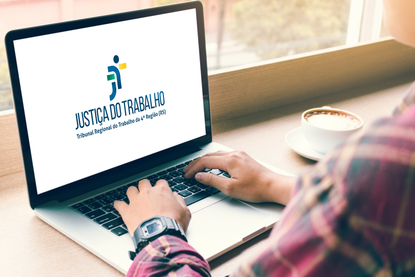 Foto de homem trabalhando em um notebook, em casa. Na tela do notebook, a logomarca do TRT4.