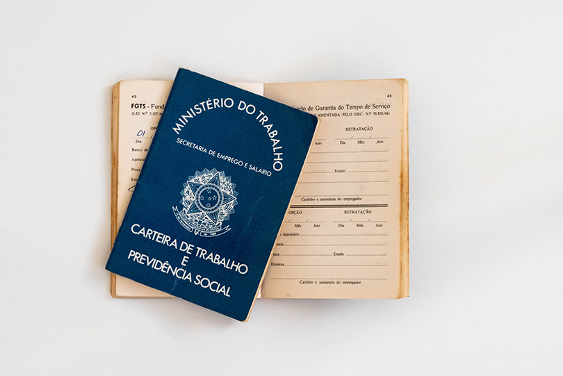 Pra Cego Ver: foto de jptinoco/iStock Banco de Imagens mostra uma Carteira de Trabalho e Previdência Social sobre outra aberta