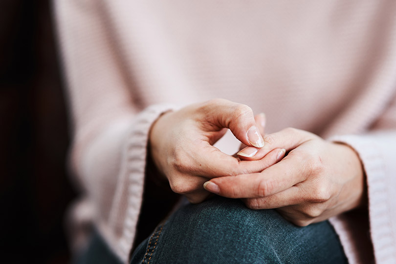 Pra Cego Ver: foto de PeopleImages/iStock Banco de Imagens mostra mulher com mãos cruzadas sobre os joelhos. Transmite a ideia de que está fazendo um desabafo/depoimento.