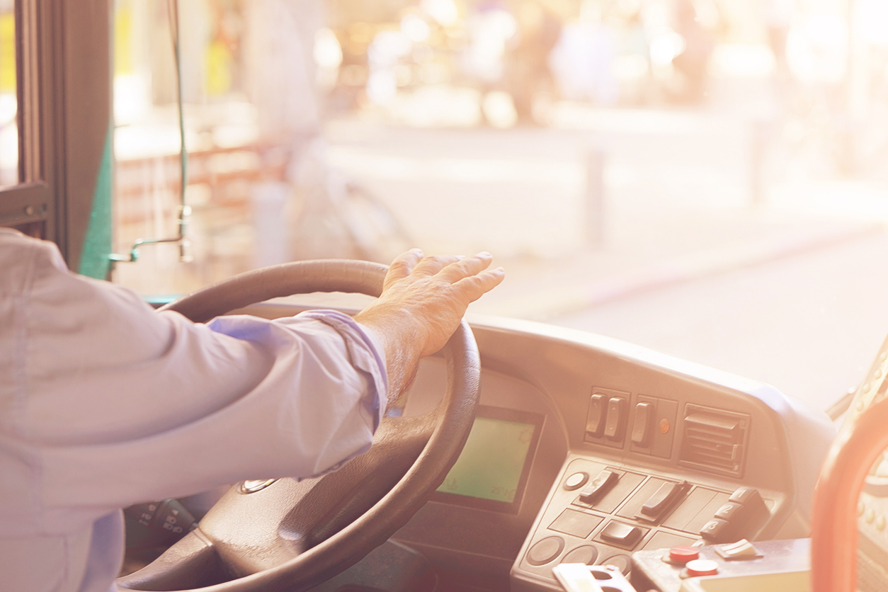 Foto da cabine de um ônibus com a mão do motorista sobre o volante
