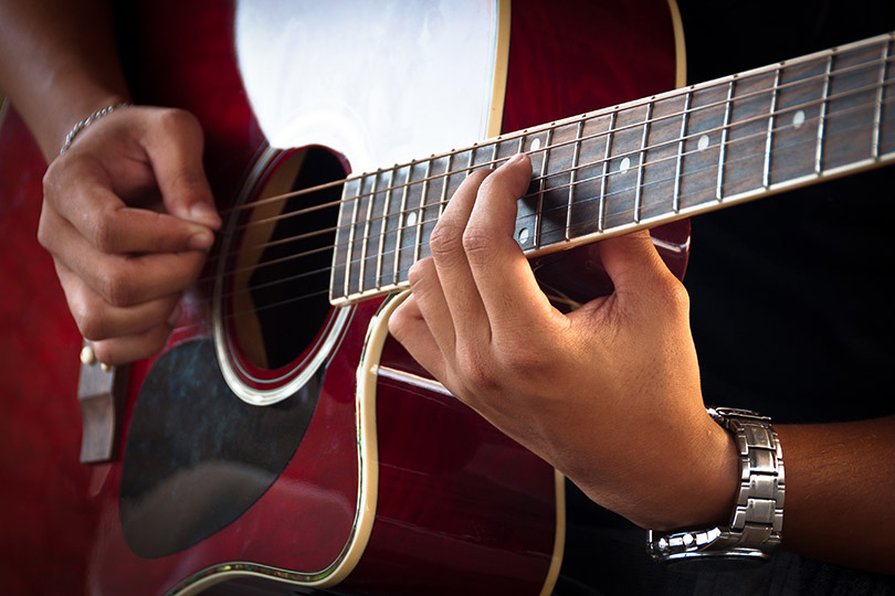 Pra Cego Ver: foto de dabldy/iStock Banco de Imagens mostra mãos de um homem negro tocando guitarra acústica.