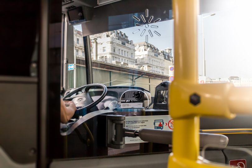 Foto ilustrativa do interior de um ônibus, mostrando ao fundo o volante e as mãos do motorista