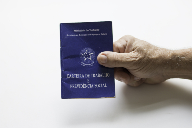 Foto ilustrativa de uma mão masculina segurando uma carteira de trabalho