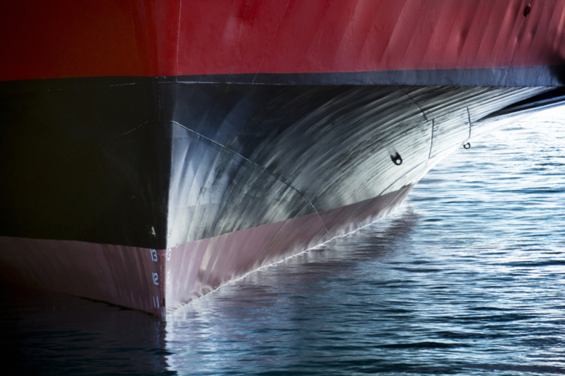 Foto ilustrativa em plano fechado de parte do casco de um navio, rodeado por água