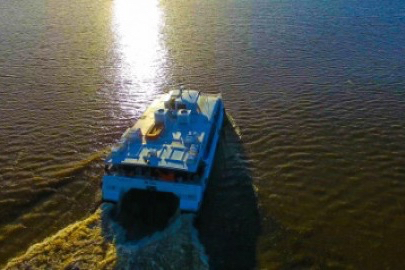 Foto área mostra uma lancha da transnorte (estilo catamarã) navegando no mar, com o reflexo do sol brilhando sobre a água.