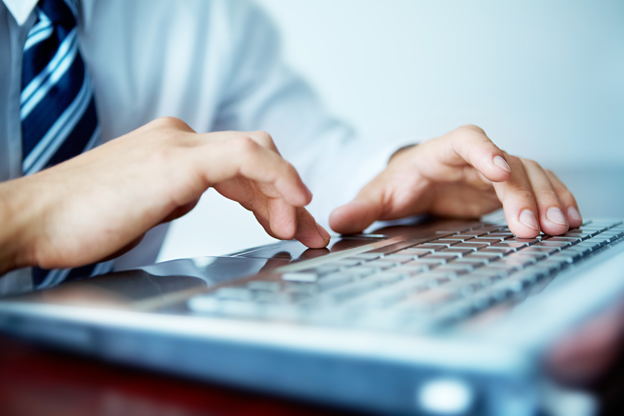 Foto ilustrativa de um homem usando camisa social e gravata digitando no teclado de um notebook.