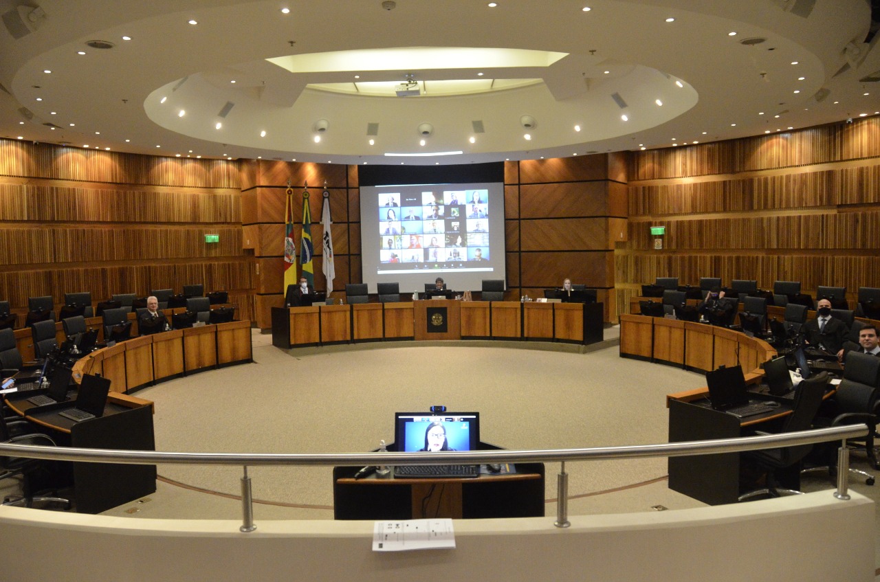 Foto em plano aberto da área central do Plenário Milton Varela Dutra, com os magistrados participando da sessão, em seus assentos, e o telão mostrando demais participantes