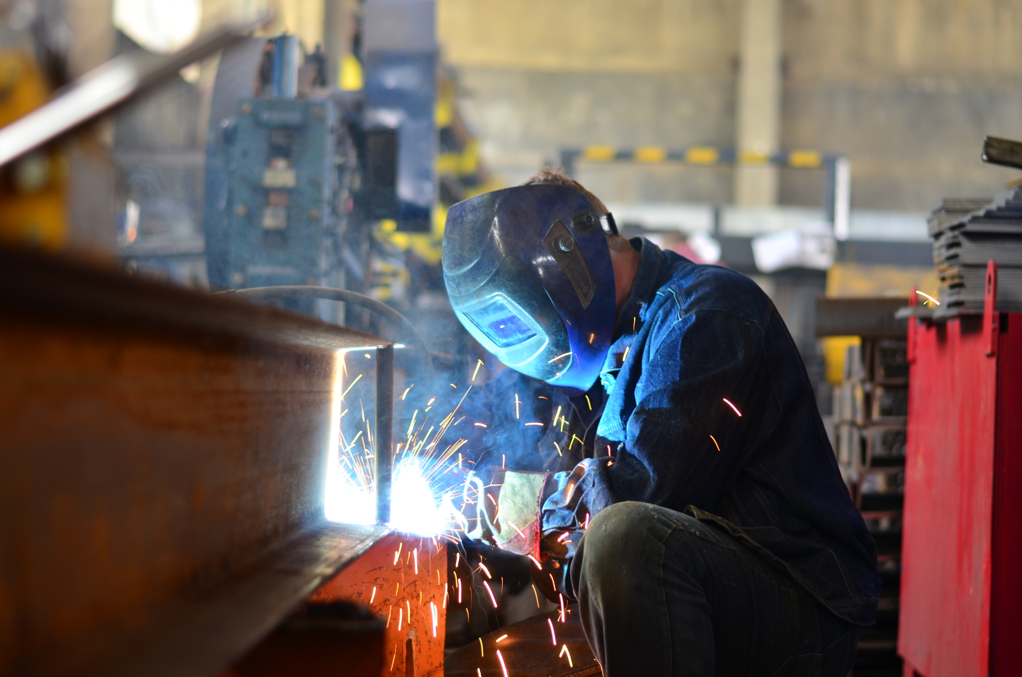 Um trabalhador em uma metalúrgica com equipamentos de proteção soldando uma peça.