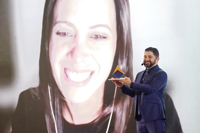 Foto da servidora Natacha sendo homenageada com a entrega simbólica do prêmio, por um dos membros do evento.