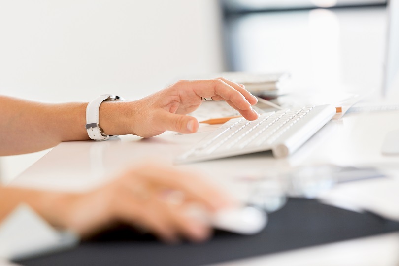 Foto ilustrativa das mãos de uma pessoa utilizando o teclado e o mouse de um computador.