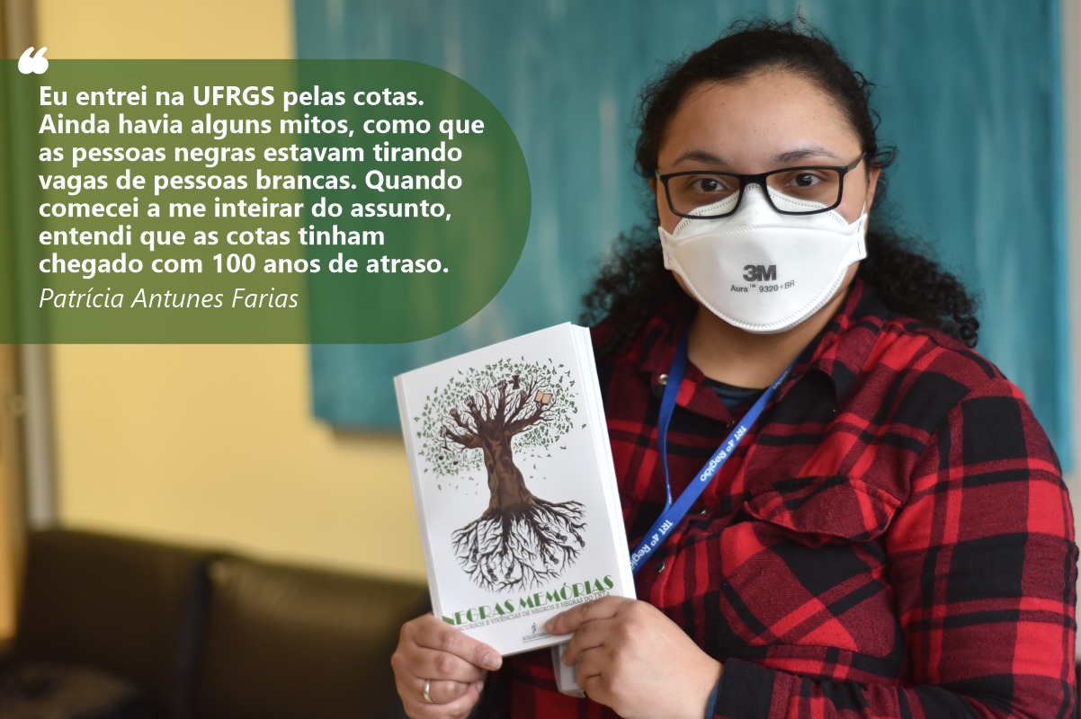 Foto de Patrícia olhando para a câmera e mostrando o livro Negras Memórias. Ela tem a pele e olhos negros. Usa óculos, uma camisa de flanela, com estampa xadrez vermelho e preto. Seus cabelos são longos e crespos e estão presos atrás da cabeça.