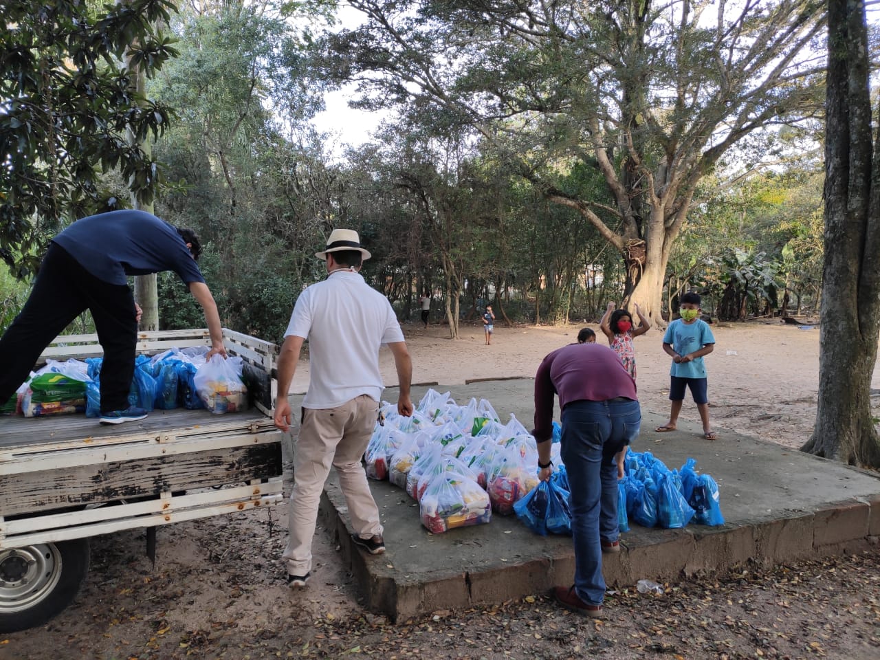 Foto mostra a entrega em uma área indígena. Há três homens retirando as cestas da carroceria de um caminhão. Três crianças indígenas observam o trabalho dos voluntários.