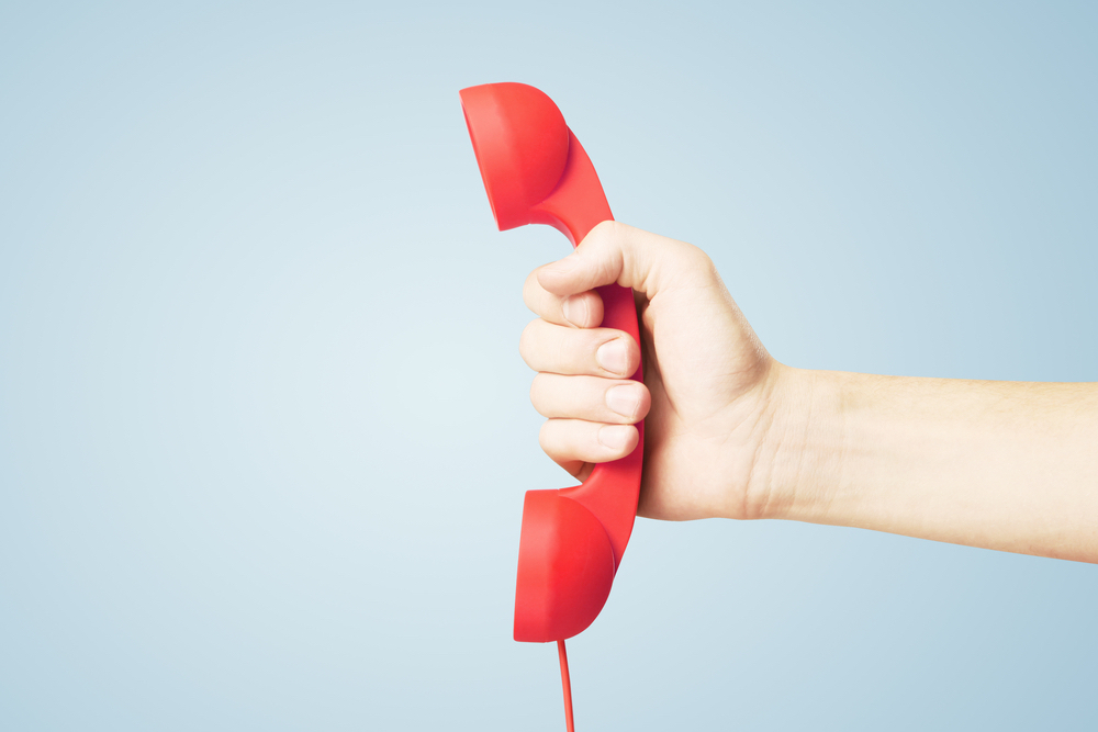Foto de uma mão segurando um telefone vermelho.