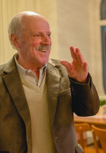 Advogado Valmor Bonfadini. Ele era um senhor alto, claro, parcialmente calvo, com bigode  e cabelos bancos. Está sorrindo. Usa casaco marrom, blusão e camisa em tons de bege.